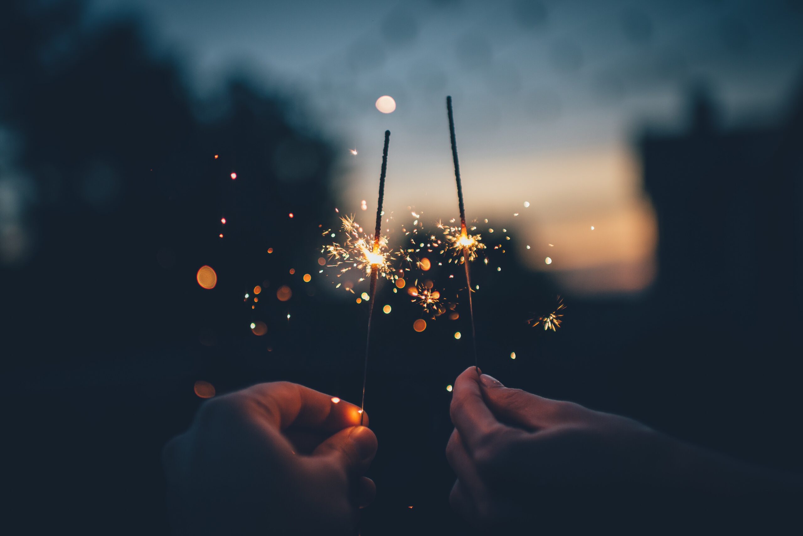 2 hands holding sparklers in the dusk